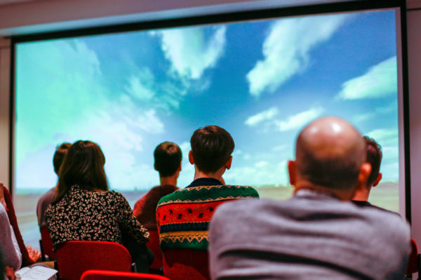 A group of people sitting down and looking at an image of clouds