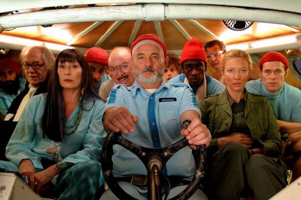 Group of people looking straight ahead with man in centre holding onto steering wheel