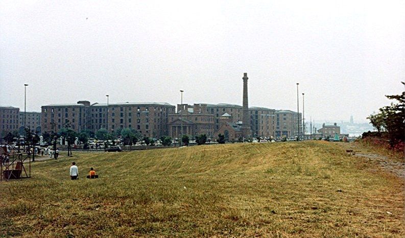 A photograph of Ambroz lake with two ducks swimming. At the back in the far distance, there is a set of flats.