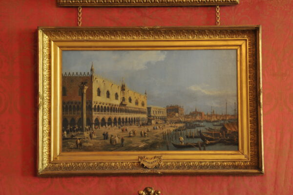 An image fo a painting, a landscape in Venice, in a gold frame and on a red wall