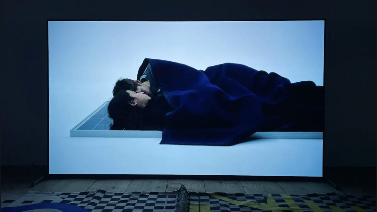 Film projected onto wall of two people lying down under a blanket.