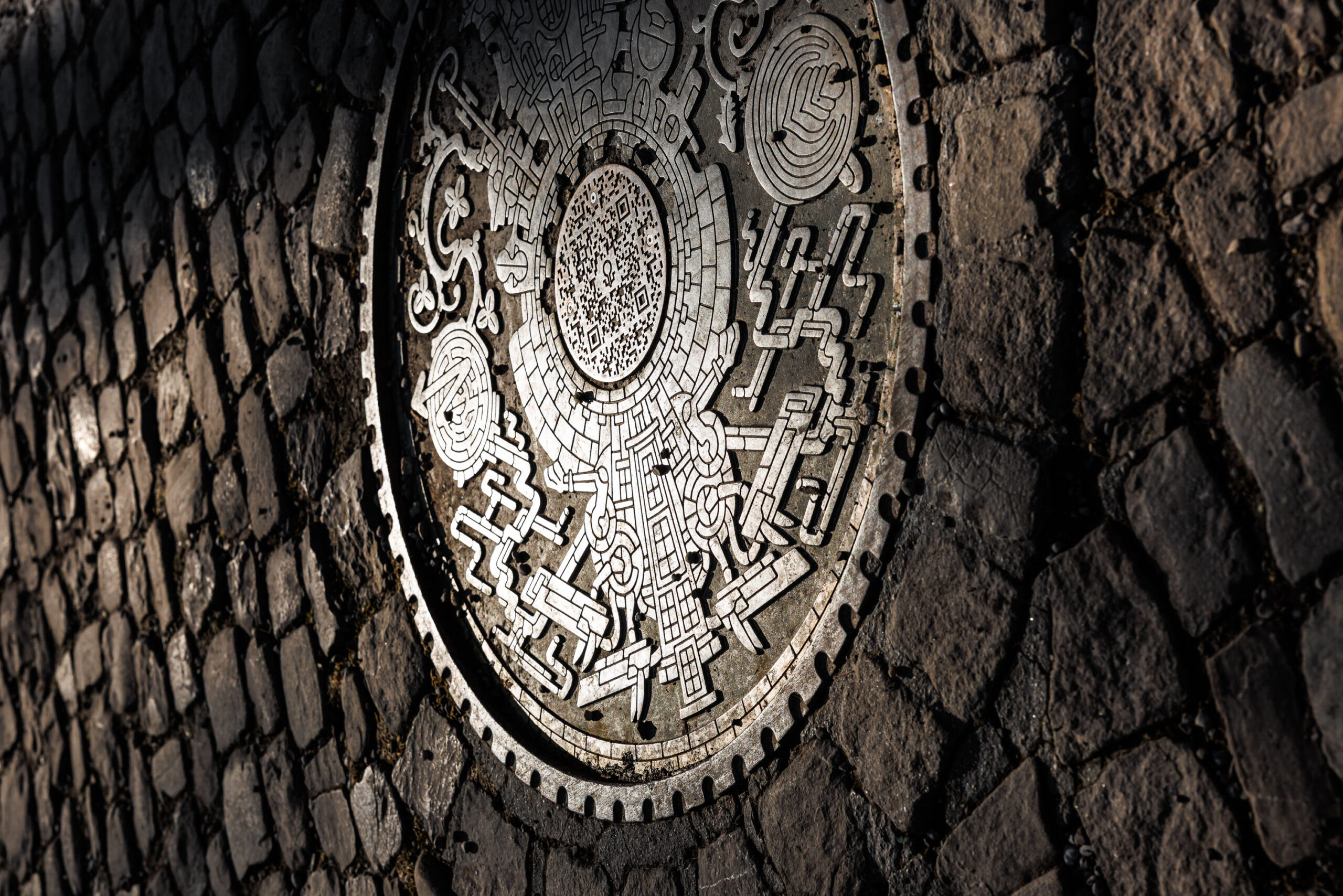 An iron nanhole cover with an intricate design on it. A QR code sits in the middle.